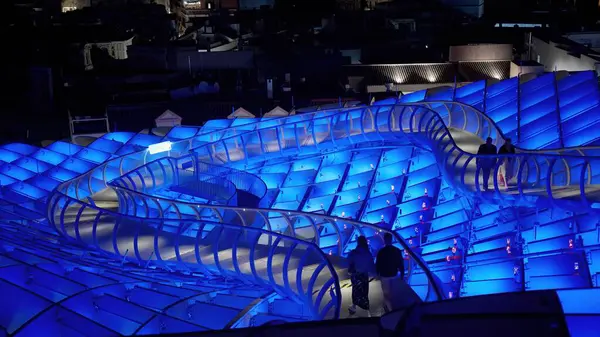 Metropol Şemsiyesi 'nin yükseltilmiş geçidi Sevilla, İspanya' da yürüyen insanlarla geceleyin mavi ışıkla aydınlanıyor - SEVILLE, SPAIN - 25 Mart 2025