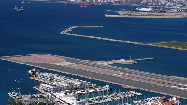 Gibraltar Uluslararası Havaalanı pistinin arka planda yelken açan marina, bina ve gemileriyle havadan görünüşü - GIBRALTAR, İngiltere - 31 Mart 2025