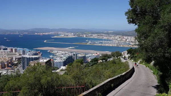 Güneşli bir günde manzaralı bir yolda yürüyen turistler, Cebelitarık Havalimanı, Algeciras Körfezi ve şehir - GIBRALTAR, İngiltere - 31 Mart 2025