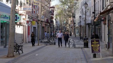 Gündüz vakti Gibraltar ana caddesinde her iki taraftaki mağazalar ve restoranlarla yürüyen insanlar - GIBRALTAR, İngiltere - 31 Mart 2025