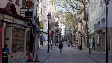 Gibraltar 'da ana caddede yürüyen bir kadın, yollar boyunca dükkanlar ve ağaçlarla kaplı - GIBRALTAR, İngiltere - 31 Mart 2025