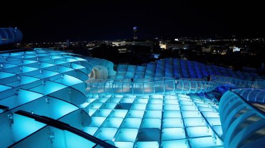 Metropol Şemsiyesi 'nden geçen yüksek yürüyüş yolu gece maviyle aydınlatılmış, arka planda Seville şehri manzarası - SEVILLE, SPAIN - 25 Mart 2025