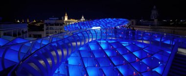 Metropol Şemsiyesi gece mavi renkte aydınlatılırken Sevilla silueti arka planda SEVILLE, SPAIN - 25 Mart 2025