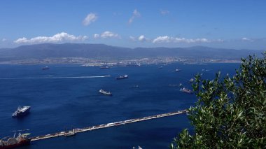 Avrupa 'nın en büyük limanı olan Algeciras, İspanya yakınlarından geçen kargo gemileri, güneşli bir günde arka planda dağlarla birlikte - GIBRALTAR, İngiltere - 31 Mart 2025