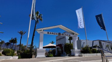 Banus Sahili 'nin beyaz girişi, rüzgarda dalgalanan bayraklar, Marbella, İspanya' da turistleri karşılama - MARBELLA, İspanya - 30 Mart 2025