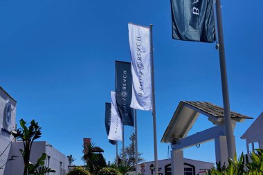 Marbella, İspanya 'da rüzgarda dalgalanan Banos Beach logosu olan beyaz ve koyu dikey bayraklar - MARBELLA, İspanya - 30 Mart 2025