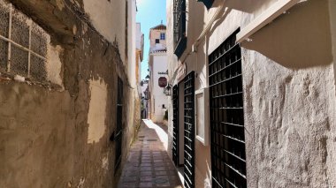 Marbella, İspanya 'da beyaz binalar ve pencerelerde parmaklıklar olan dar bir sokakta parlayan güneş - MARBELLA, İspanya - 30 Mart 2025