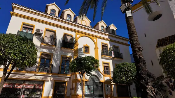 Güneşli bir günde İspanya, Marbella 'da palmiye ağaçlarının gölgeleriyle geleneksel beyaz ve sarı bina cephesi - MARBELLA, SPAIN - 30 Mart 2025
