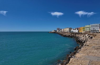 İspanya, Cadiz 'in renkli binaları, güneşli bir günde dalgalı sulardan görünen Atlantik Okyanusu kıyıları boyunca uzanır.