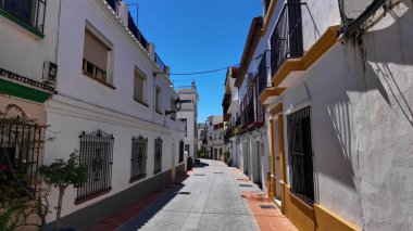 Geleneksel beyazlatılmış binalar İspanya 'nın Marbella şehrinde dar bir cadde boyunca uzanır ve parlak yaz güneşi altında güzel bir manzara yaratır.