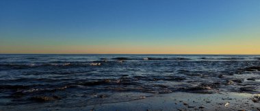 Gün batımında açık mavi gökyüzüyle Marbella sahilini yıkayan küçük dalgalar.