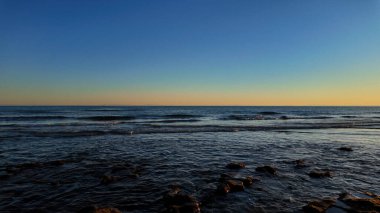 İspanya, Marbella 'da gün batımında sakin deniz dalgaları yavaşça kıyıya vuruyor.