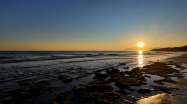 Güneş ufukta batıyor İspanya 'daki Marbella sahilinin ıslak kayalarında altın yansımalar yaratıyor.