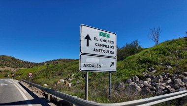 İspanya 'nın Endülüs dağlarındaki dolambaçlı bir yolun yakınında El Chorro, Campillos, Antequera ve Ardales' e giden yolu gösteren yol tabelası.
