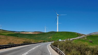 Rüzgar türbinleri açık mavi gökyüzünün altında yeşil bir yamaçta