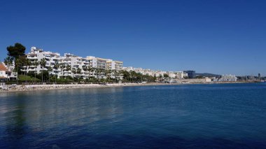 Marbella İspanya 'da Estepona sahilinin beyaz binalarını ve palmiye ağaçlarını yansıtan berrak mavi gökyüzünün altında sakin bir Akdeniz.