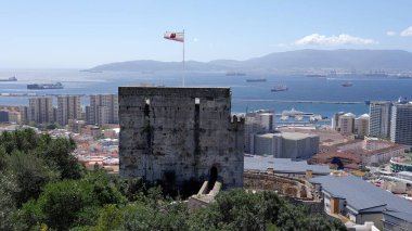 Mağribi Kalesi rüzgarda dalgalanan Cebelitarık bayrağını sergiliyor, mavi gökyüzü ve deniz arka planda