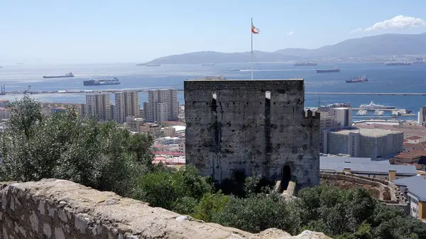 Gibraltar bayrağı şehirle birlikte bir Fas şatosunun üzerinde dalgalanırken arka planda liman ve Akdeniz 'de yelken açan kargo gemileri