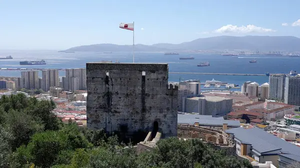 Mağribi Kalesi rüzgarda dalgalanan Cebelitarık bayrağını sergiliyor, mavi gökyüzü ve deniz arka planda