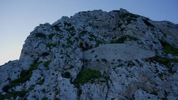 Cebelitarık Kayası 'nın alçak açılı manzarası alacakaranlığın yumuşak ışığıyla aydınlanan dik kayalık bir dağ yamacına inşa edilmiş antik taş bir duvar.