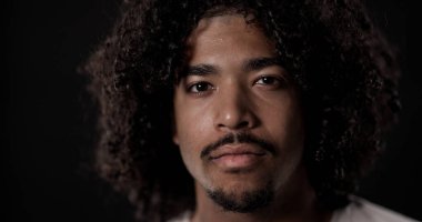 Kıvırcık saçlı ve keçi sakallı, koyu renk bir arka plana karşı yoğunluğunu ifade eden ciddi bir Afro-Amerikalı adamın portresini yakından çek.