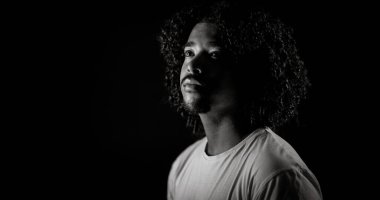 Kıvırcık saçlı Afro-Amerikan genç bir adamın dramatik siyah beyaz portresi.