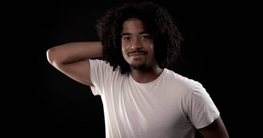 Siyah arka planda gülümseyen kıvırcık saçlı Afro-Amerikan bir adamın stüdyo portresi.