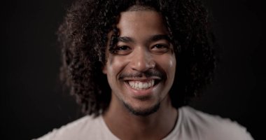 Siyah arka planda gülümseyen kıvırcık saçlı Afro-Amerikan bir adamın portresi.