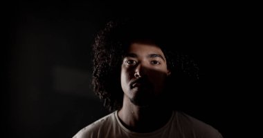 Siyahi Amerikalı genç bir adamın dramatik portresi. Kıvırcık saçlı, açık renkli bir kaynaktan kısmen aydınlatılmış.