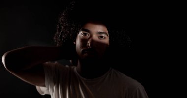 Bir ışık demeti tarafından kısmen aydınlatılmış genç bir Afro-Amerikan 'ın dramatik portresi anımsatıcı ve gizemli bir atmosfer yaratıyor.