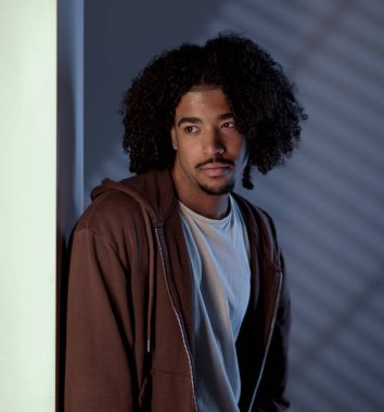 Dalgın, genç, Afro-Amerikalı, kıvırcık saçlı, duvara yaslanmış ve gözlerini çevirmiş.