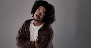 Stüdyoda poz veren kıvırcık saçlı ve çapraz kollu Afro-Amerikalı genç bir adamın portresi.