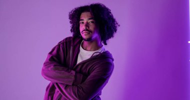 Mor neon ışıkların altında çapraz kollarla poz veren modaya uygun dansçı, modern tarz ve kendine güven sergiliyor.