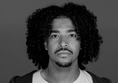 Kıvırcık saçlı ve keçi sakallı, stüdyo ortamında poz veren ciddi bir Afro-Amerikan 'ın siyah beyaz portresi.