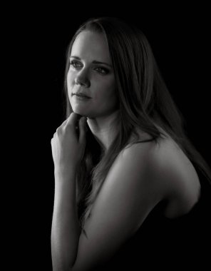 Güzel, düşünceli bir kadının siyah beyaz portresi. Çenesini eliyle tutuyor, karanlık bir arka plana bakıyor.