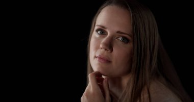 Uzun kahverengi saçlı güzel bir kadın. Siyah arka planda elleri çenesinde poz veriyor.