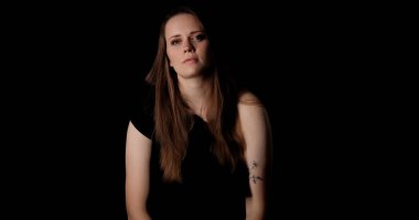 Uzun kahverengi saçlı ve sol kolunda çiçek dövmesi olan genç bir kadının stüdyo portresi.