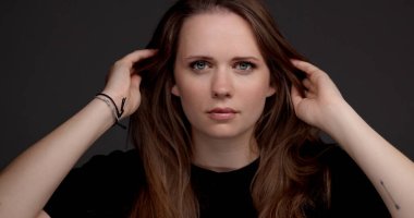 Saçına gri arka planda dokunan genç bir kadının stüdyo portresi.