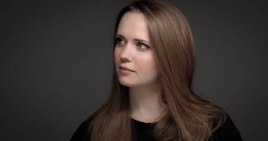 Stüdyo portresi, uzun kahverengi saçlı güzel bir kadının gri arka planda kameradan uzağa bakması.