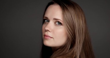 Stüdyo portresi, uzun kahverengi saçlı güzel bir kadının gri arka planda arkasını kollaması.