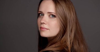 Stüdyo portresi, uzun kahverengi saçlı güzel bir kadının gri arka planda arkasını kollaması.