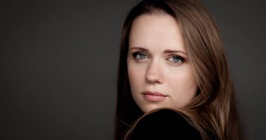 Stüdyo portresi, kahverengi saçlı, mavi gözlü, siyah gömlekli, koyu bir arka planda omzunun üzerinden bakan güzel bir beyaz kadın.