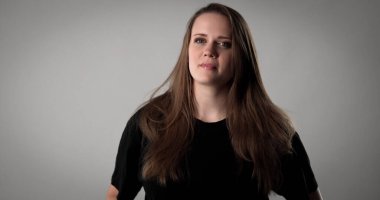 Uzun kahverengi saçlı, siyah tişörtlü, kendine güveni ve tarzı olan güzel bir kadının stüdyo portresi.