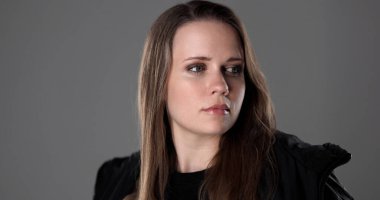 Uzun saçlı, gri arkaplana bakan ciddi bir genç kadının stüdyo portresi.