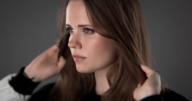 Saçlarıyla gri bir arka planda oynayan güzel bir genç kadının stüdyo portresi.