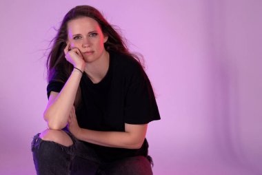 Canlı bir stüdyoda renkli bir arka planda poz veren düşünceli genç bir kadın çarpıcı bir görüntü yaratıyor.