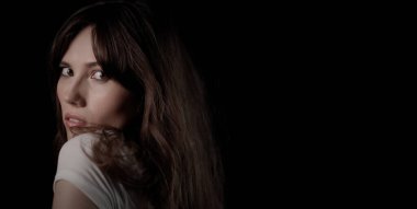 Uzun kahverengi saçlı güzel bir kadın siyah bir arka planda arkasını kolluyor.