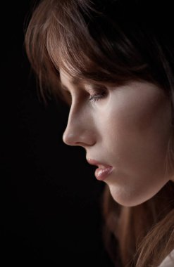 Doğal makyajlı ve siyah arkaplanda poz veren güzel bir genç kadın profili.