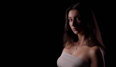 Uzun kahverengi saçlı, straplez bluz ve kolyeli esmer bir kadının stüdyo portresi.