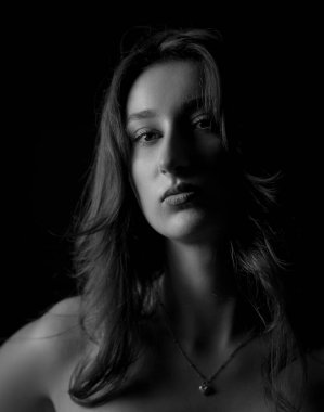 Uzun saçlı, siyah arka planda kolye takan güzel bir genç kadının stüdyo portresi.